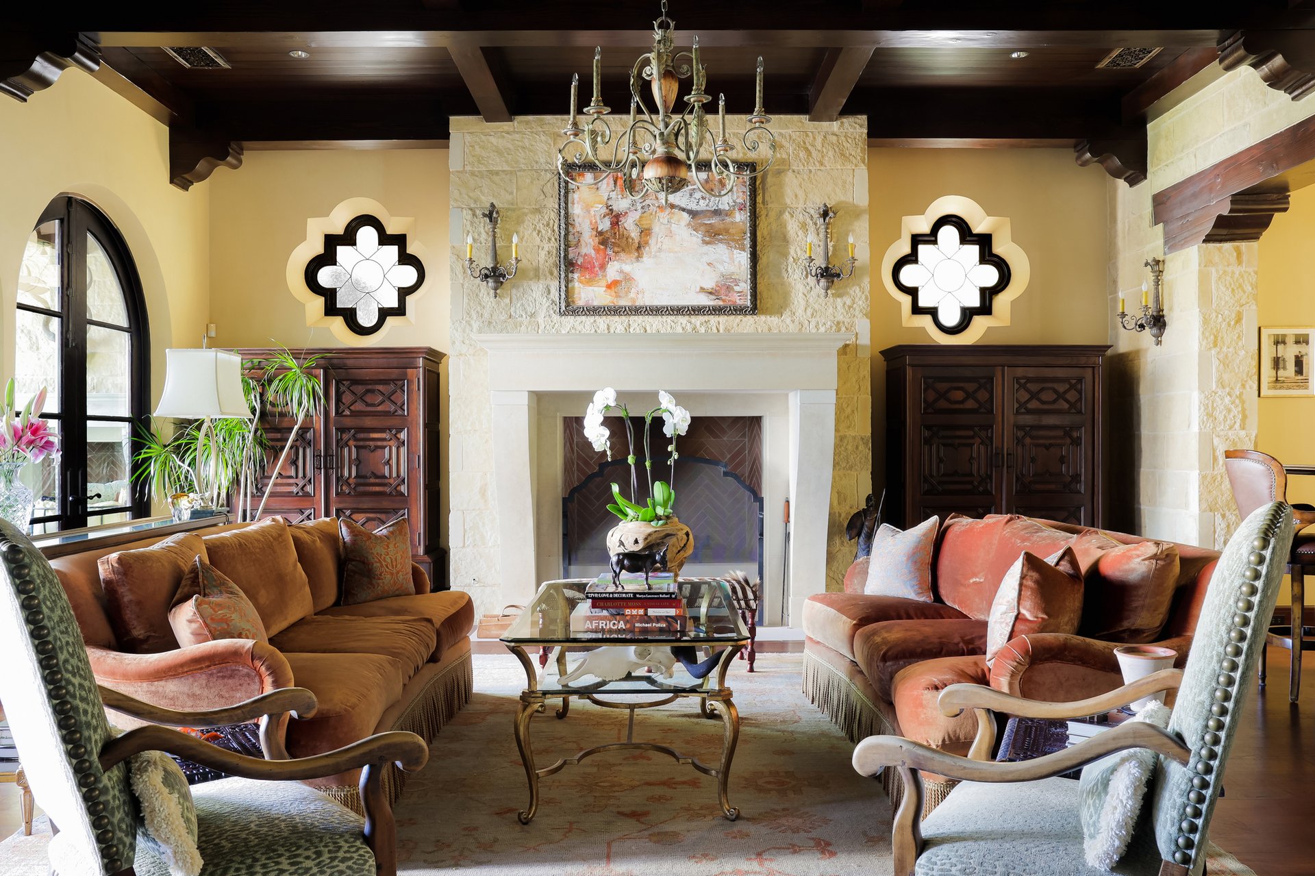 Living room with stone fireplace, antique chandelier, and velvet sofas